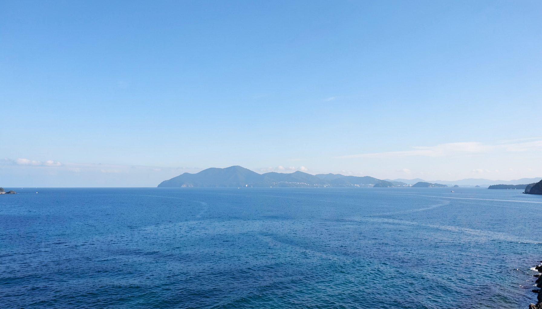 日本列島を思わせる穏やかな海岸線の風景、青い空と海が広がる落ち着いた色調
